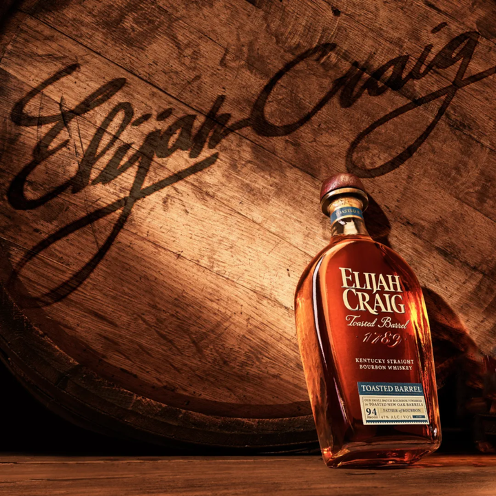 Bottle of Elijah Craig Toasted Barrel bourbon whiskey on a wooden barrel with the brand name visible.