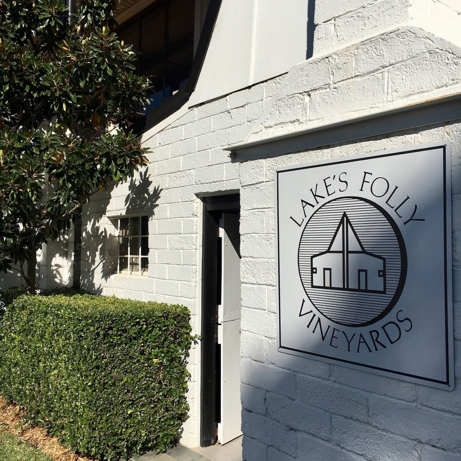 Lake's Folly Vineyards sign on a white brick building with greenery.