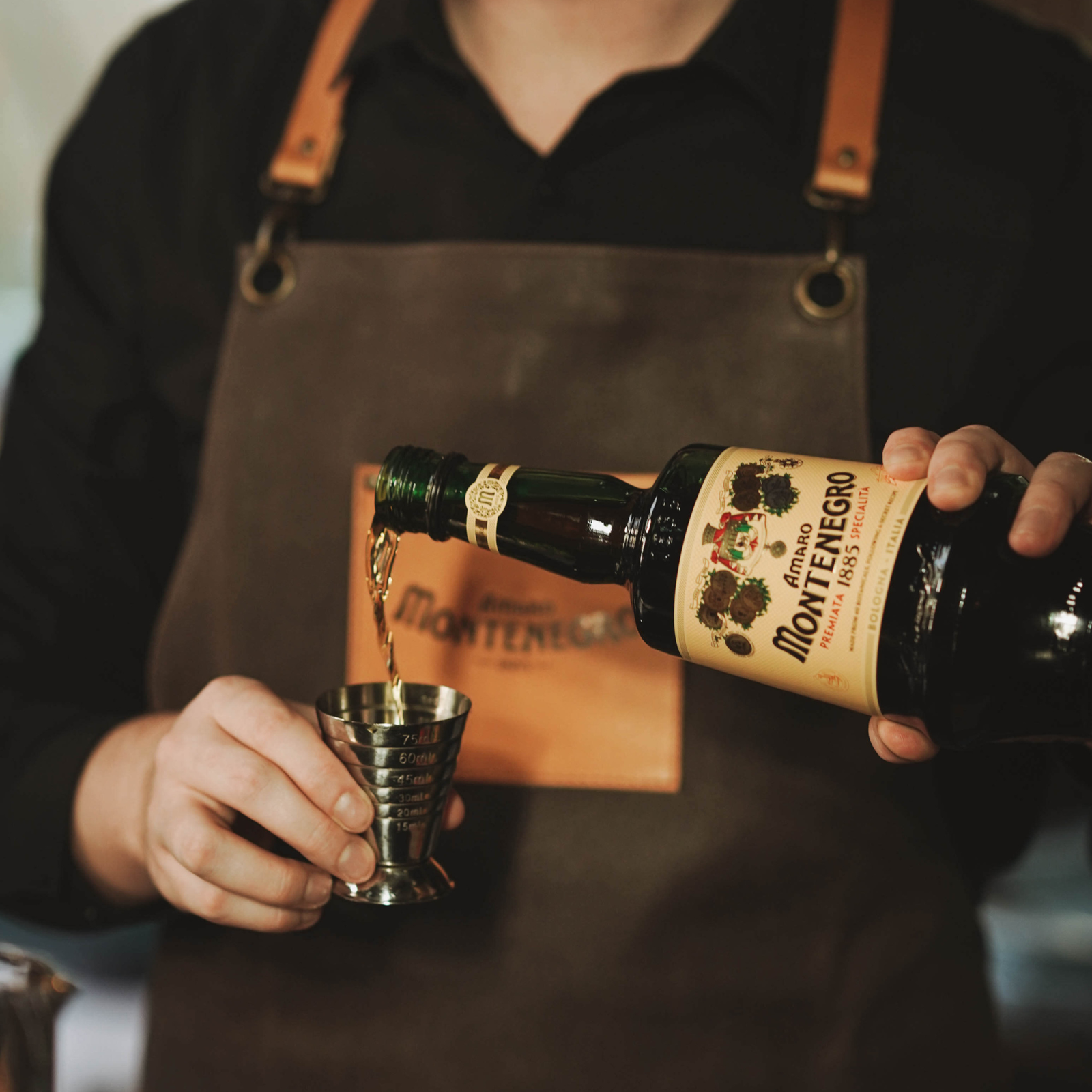 Person pouring Montenegro brand liquor into a glass with a focus on the bottle and apron.