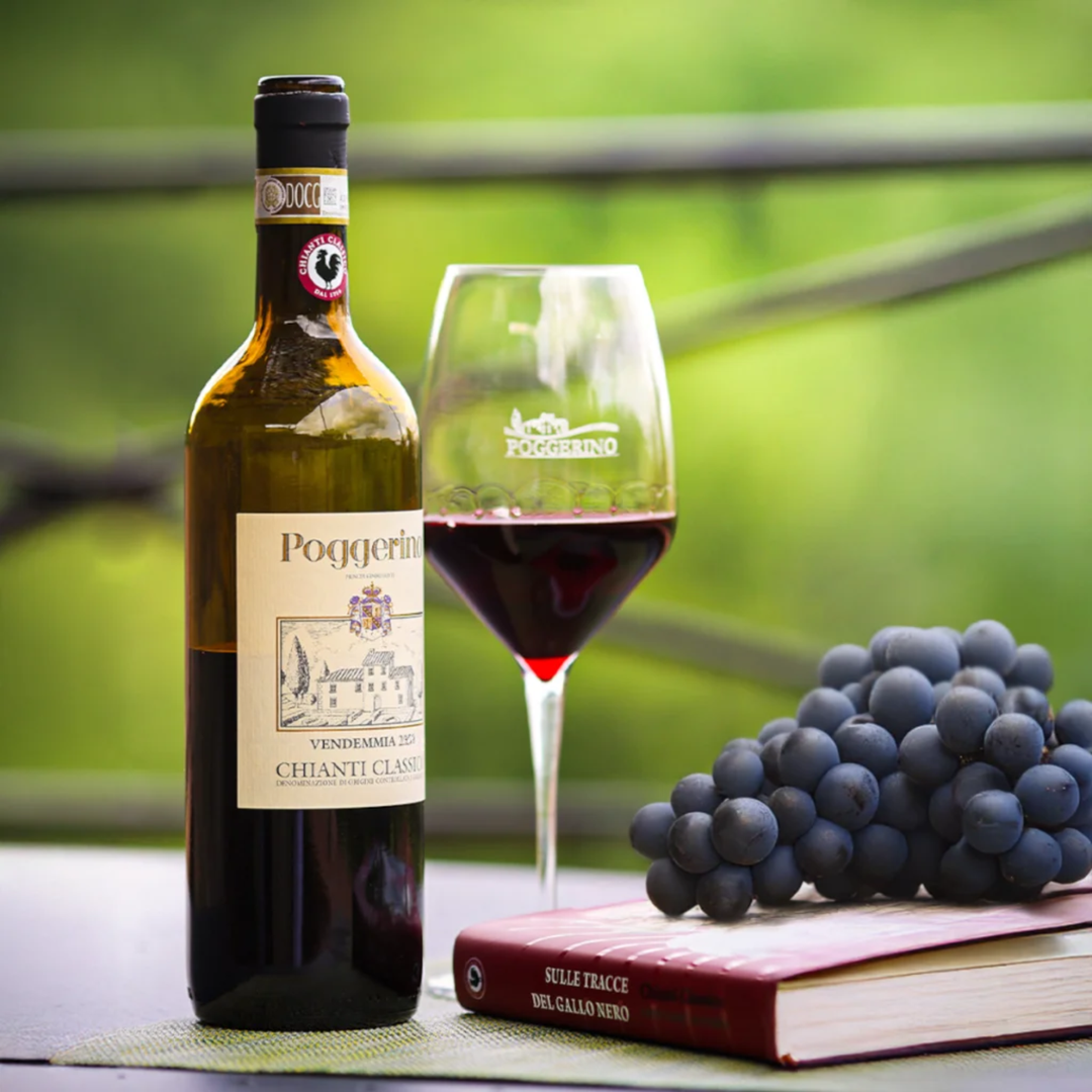 A bottle of Poggellerino Chianti Classico 2024 red wine stands beside a filled wine glass, a bunch of dark grapes, and a red book on a table with a blurred green outdoor background.